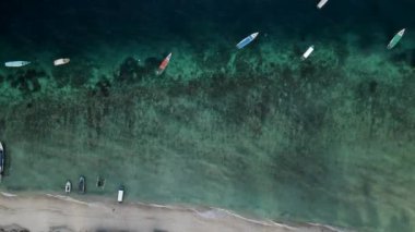 Nusa Ceningan Bali Endonezya 'daki Çapalı Oturan Teknelerle Kristal Berrak Mavi Sahil Suyu boyunca uçmak, sahil boyunca okyanusta yüzen tekneleri göstermek. Yelkenli bir teknenin havadan görünüşü