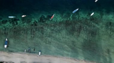 Nusa Ceningan Bali Endonezya 'daki Çapalı Oturan Teknelerle Kristal Berrak Mavi Sahil Suyu boyunca uçmak, sahil boyunca okyanusta yüzen tekneleri göstermek. Yelkenli bir teknenin havadan görünüşü