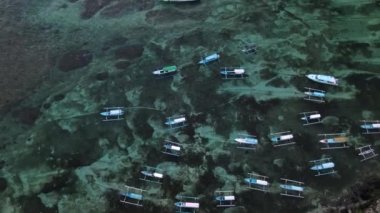 Nusa Ceningan Bali Endonezya 'daki Çapalı Oturan Teknelerle Kristal Berrak Mavi Sahil Suyu boyunca uçmak, sahil boyunca okyanusta yüzen tekneleri göstermek. Yelkenli bir teknenin havadan görünüşü