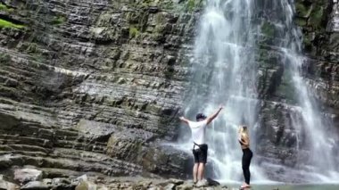 Büyük Şelale 'ye bakan mutlu genç çift, Büyük Şelale' ye bakan mutlu genç çift. Turist dağlardaki şelaleyi ziyaret ediyor. Seyahat, aktif yaşam tarzı seyahat insanlar arka planda duruyor güzel şelale, şelalenin yanında duruyor.