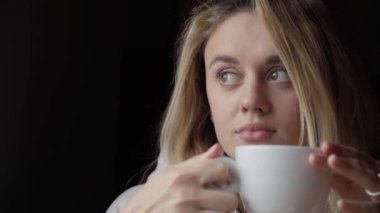  Kahve içen genç bir kadın, modaya uygun giysiler içindeki güzel bir kadın kafede kahve içiyor yalnızlığın ve lezzetli içkinin tadını çıkarıyor masada tek başına oturup pencereden dışarı bakıp içen bir kız.