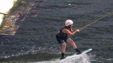 Çocuk uyanma parkındaki gölette kablo yaylım tahtasıyla meşgul. Aarhus, Danimarka - 05.21.2023, Çocuk uyanma parkındaki gölette kablo wakeboard ile meşgul. Kafkasyalı genç adam şehir gölünde wakeboard 'unda numaralar yapıyor.