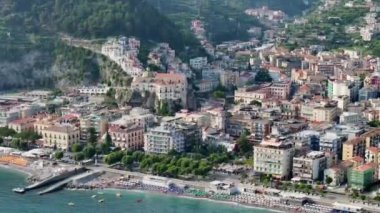 Maiori, İtalya 'da birçok sandalye ve şemsiyeyle modern bir plaj manzarası. Amalfi 'deki temiz şeffaf turkuaz akdeniz suyuyla büyük bir sahil sahilinde dinlenen insanların insansız hava aracı görüntüsü.