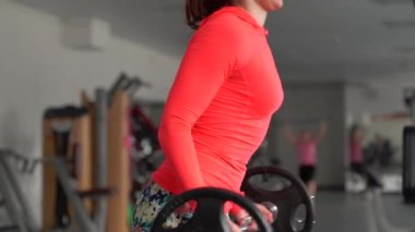 Takım fitness kızı vücut geliştirme, halter kız beden eğitimi, spor kadın antrenmanı. Genç bir kadın spor salonundaki aynanın önünde spor aletleriyle eğilim gösteriyor. 