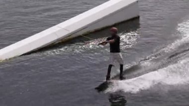 Wakeboardcu parktaki kablo TV 'de, açık havada suyla aşırı ilgilenen, suda sörf yapan, nehirde wakeboard kullanan genç bir adam., 