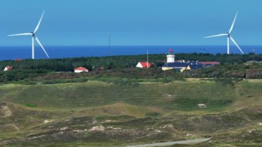 Gün batımında bir rüzgar çiftliğinin drone görüntüsü. Çoklu rüzgar türbinleri, güzel güneşli yaz sonbahar karasularında rüzgar türbinleri. Dağdan geçen kıvrımlı bir yol. Yeşil ekolojik enerji üretimi.