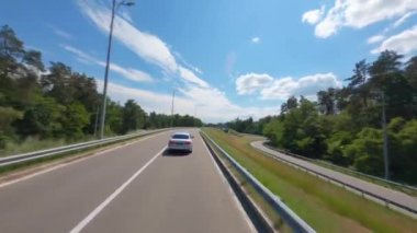 FPV, araba yola çıkıyor. Karışık orman. Yol gezisi, otoyolda giden iş arabası, ormanın arka planına doğru giden araba, arabalı doğa. Arabayla manzara, ulaşım 