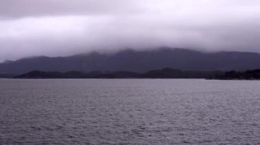 Norveç 'te gezinti. Bottan fiyordun manzarası, tekneden dağların manzarası, şelaleler, yolcu gemileri ve hassas tekneler turistleri gemiden kıyıya taşıyan mavi gökyüzü ile güzel bir günde