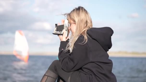カメラ付きハッピーガール 少女は海岸の岩の上に座ってヴィンテージレトロカメラの風景に写真を撮る美しい若い旅行者です 自然へのバックパックとカメラで旅行 — ストック動画
