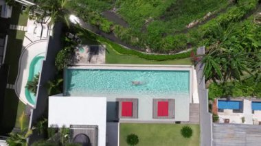 Bir adam havuzunda dinleniyor, lüks bir yüzme havuzunda tek başına yüzüyor, yüzücü adam lüks bir villada havuza dalıyor. Havadan çekim. Dikkatsiz yaz tatili imajı. tatil 