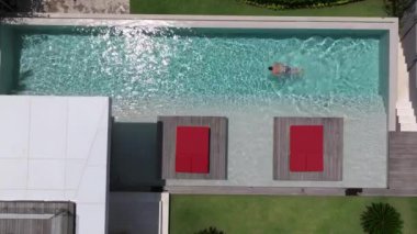 Bir adam havuzunda dinleniyor, lüks bir yüzme havuzunda tek başına yüzüyor, yüzücü adam lüks bir villada havuza dalıyor. Havadan çekim. Dikkatsiz yaz tatili imajı. tatil 