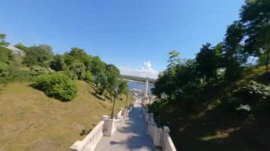 FPV drone, Reunion Arch, Kyiv: Halkın Dostluk Kemeri ve Volodymyr Hill Köprüsü. Kiev 'deki parkın ve yaya köprüsünün manzarası. Parktaki insanlar ve yeşil ağaçlar. Drone Video. Ukrayna. Avrupa