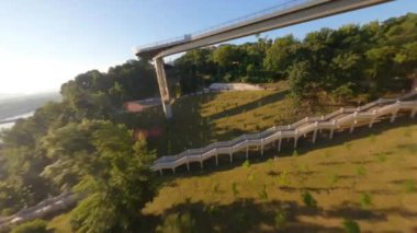 FPV drone, Reunion Arch, Kyiv: Halkın Dostluk Kemeri ve Volodymyr Hill Köprüsü. Kiev 'deki parkın ve yaya köprüsünün manzarası. Parktaki insanlar ve yeşil ağaçlar. Drone Video. Ukrayna. Avrupa
