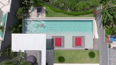 Bir adam havuzunda dinleniyor, lüks bir yüzme havuzunda tek başına yüzüyor, yüzücü adam lüks bir villada havuza dalıyor. Havadan çekim. Dikkatsiz yaz tatili imajı. tatil 