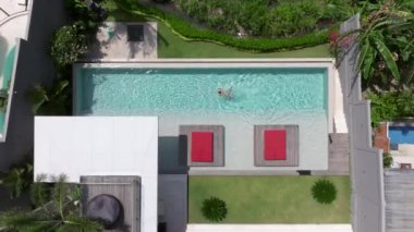 Bir adam havuzunda dinleniyor, lüks bir yüzme havuzunda tek başına yüzüyor, yüzücü adam lüks bir villada havuza dalıyor. Havadan çekim. Dikkatsiz yaz tatili imajı. tatil 