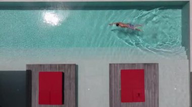 Bir adam havuzunda dinleniyor, lüks bir yüzme havuzunda tek başına yüzüyor, yüzücü adam lüks bir villada havuza dalıyor. Havadan çekim. Dikkatsiz yaz tatili imajı. tatil 