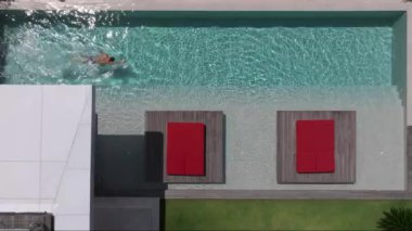 Bir adam havuzunda dinleniyor, lüks bir yüzme havuzunda tek başına yüzüyor, yüzücü adam lüks bir villada havuza dalıyor. Havadan çekim. Dikkatsiz yaz tatili imajı. tatil 