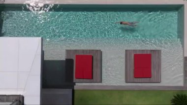 Bir adam havuzunda dinleniyor, lüks bir yüzme havuzunda tek başına yüzüyor, yüzücü adam lüks bir villada havuza dalıyor. Havadan çekim. Dikkatsiz yaz tatili imajı. tatil 