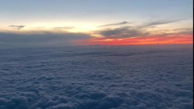 Bir uçağın penceresinden dışarı bakmak, Bulutlar, ufukta güneş doğarken uçaktan manzara 