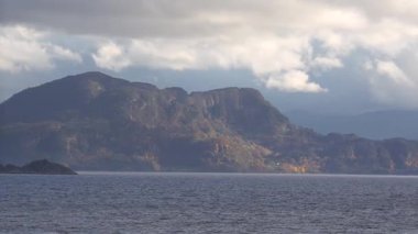 Norveç 'te gezinti. Bottan fiyordun manzarası, tekneden dağların manzarası, şelaleler, yolcu gemileri ve hassas tekneler turistleri gemiden kıyıya taşıyan mavi gökyüzü ile güzel bir günde