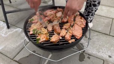 Barbeküde taze otlarla et pişiren bir kadın parti için domuz pastırmalı baharatlı sosisli piknik yapan bir kadın. Izgara domuz eti ateşte yanıyor.