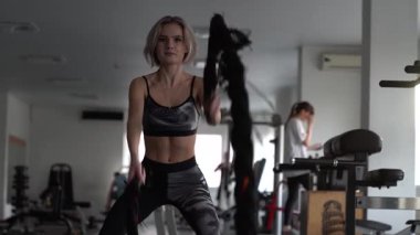SstkWellness, Sporcu kız spor salonundaki halatlarla fitness antrenmanına odaklandı. Çekici, formda, sporcu bir kadın. Spor salonunda çalışıyor. Savaş halatlarıyla egzersiz yapıyor..