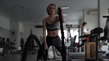 SstkWellness, Sporcu kız spor salonundaki halatlarla fitness antrenmanına odaklandı. Çekici, formda, sporcu bir kadın. Spor salonunda çalışıyor. Savaş halatlarıyla egzersiz yapıyor..