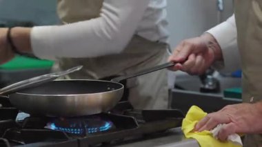 Ticari bir mutfakta çalışan profesyonel bir aşçı yemek pişirme tavaları ve diğer mutfak malzemelerinden yükselen buharlı bir yemek hazırlıyor.