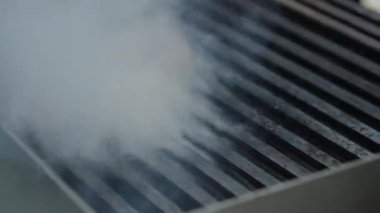 Ticari bir mutfakta çalışan profesyonel bir aşçı yemek pişirme tavaları ve diğer mutfak malzemelerinden yükselen buharlı bir yemek hazırlıyor.