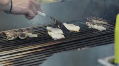 Ticari bir mutfakta çalışan profesyonel bir aşçı yemek pişirme tavaları ve diğer mutfak malzemelerinden yükselen buharlı bir yemek hazırlıyor.