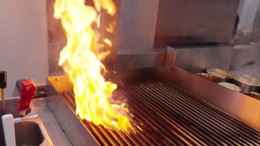 Ticari bir mutfakta çalışan profesyonel bir aşçı yemek pişirme tavaları ve diğer mutfak malzemelerinden yükselen buharlı bir yemek hazırlıyor.