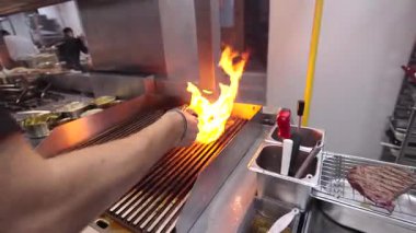 Ticari bir mutfakta çalışan profesyonel bir aşçı yemek pişirme tavaları ve diğer mutfak malzemelerinden yükselen buharlı bir yemek hazırlıyor.