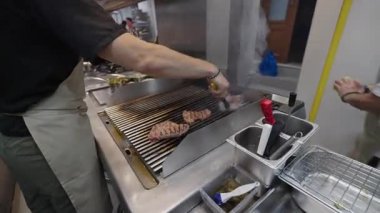 Ticari bir mutfakta çalışan profesyonel bir aşçı yemek pişirme tavaları ve diğer mutfak malzemelerinden yükselen buharlı bir yemek hazırlıyor.