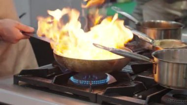 Ticari bir mutfakta çalışan profesyonel bir aşçı yemek pişirme tavaları ve diğer mutfak malzemelerinden yükselen buharlı bir yemek hazırlıyor.