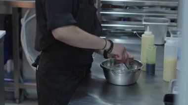 Ticari bir mutfakta çalışan profesyonel bir aşçı yemek pişirme tavaları ve diğer mutfak malzemelerinden yükselen buharlı bir yemek hazırlıyor.