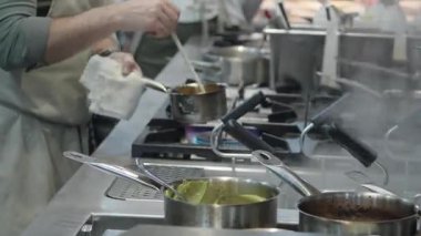 Ticari bir mutfakta çalışan profesyonel bir aşçı yemek pişirme tavaları ve diğer mutfak malzemelerinden yükselen buharlı bir yemek hazırlıyor.