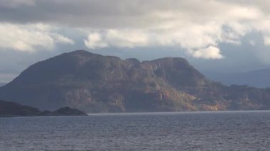 Norveç 'te gezinti. Bottan fiyordun manzarası, tekneden dağların manzarası, şelaleler, yolcu gemileri ve hassas tekneler turistleri gemiden kıyıya taşıyan mavi gökyüzü ile güzel bir günde