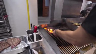 Ticari bir mutfakta çalışan profesyonel bir aşçı yemek pişirme tavaları ve diğer mutfak malzemelerinden yükselen buharlı bir yemek hazırlıyor.