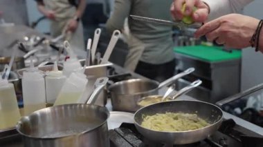Ticari bir mutfakta çalışan profesyonel bir aşçı yemek pişirme tavaları ve diğer mutfak malzemelerinden yükselen buharlı bir yemek hazırlıyor.