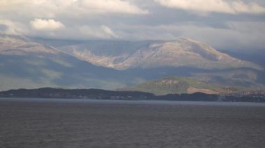 Norveç 'te gezinti. Bottan fiyordun manzarası, tekneden dağların manzarası, şelaleler, yolcu gemileri ve hassas tekneler turistleri gemiden kıyıya taşıyan mavi gökyüzü ile güzel bir günde