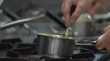 Ticari bir mutfakta çalışan profesyonel bir aşçı yemek pişirme tavaları ve diğer mutfak malzemelerinden yükselen buharlı bir yemek hazırlıyor.
