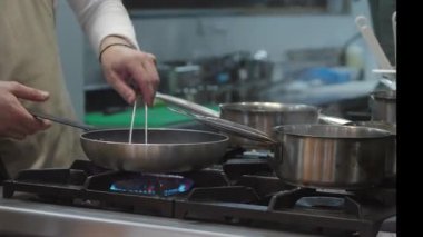 Ticari bir mutfakta çalışan profesyonel bir aşçı yemek pişirme tavaları ve diğer mutfak malzemelerinden yükselen buharlı bir yemek hazırlıyor.