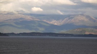 Norveç 'te gezinti. Bottan fiyordun manzarası, tekneden dağların manzarası, şelaleler, yolcu gemileri ve hassas tekneler turistleri gemiden kıyıya taşıyan mavi gökyüzü ile güzel bir günde