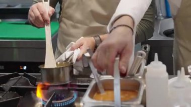 Ticari bir mutfakta çalışan profesyonel bir aşçı yemek pişirme tavaları ve diğer mutfak malzemelerinden yükselen buharlı bir yemek hazırlıyor.