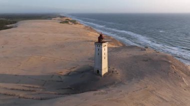 Tepenin tepesinde ünlü deniz feneri olan dev kum tepelerinin hava manzarası. Rubjerg Knude Deniz Feneri, Kuzey Deniz Rubjerg, Danimarka Lokken yakınlarındaki Rubjerg Knude Fyr deniz fenerinde gün batımı. 