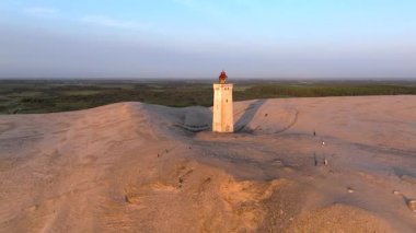Tepenin tepesinde ünlü deniz feneri olan dev kum tepelerinin hava manzarası. Rubjerg Knude Deniz Feneri, Kuzey Deniz Rubjerg, Danimarka Lokken yakınlarındaki Rubjerg Knude Fyr deniz fenerinde gün batımı. 