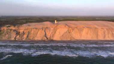 Tepenin tepesinde ünlü deniz feneri olan dev kum tepelerinin hava manzarası. Rubjerg Knude Deniz Feneri, Kuzey Deniz Rubjerg, Danimarka Lokken yakınlarındaki Rubjerg Knude Fyr deniz fenerinde gün batımı. 