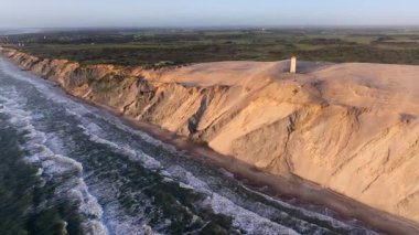 Tepenin tepesinde ünlü deniz feneri olan dev kum tepelerinin hava manzarası. Rubjerg Knude Deniz Feneri, Kuzey Deniz Rubjerg, Danimarka Lokken yakınlarındaki Rubjerg Knude Fyr deniz fenerinde gün batımı. 