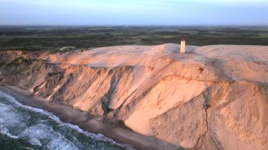 Tepenin tepesinde ünlü deniz feneri olan dev kum tepelerinin hava manzarası. Rubjerg Knude Deniz Feneri, Kuzey Deniz Rubjerg, Danimarka Lokken yakınlarındaki Rubjerg Knude Fyr deniz fenerinde gün batımı. 