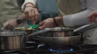 Ticari bir mutfakta çalışan profesyonel bir aşçı yemek pişirme tavaları ve diğer mutfak malzemelerinden yükselen buharlı bir yemek hazırlıyor.